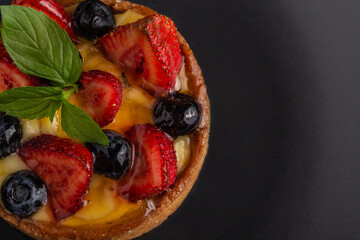Sweet cake or tart with berries and mint leaves on black plate, close up view and space for text, macro photo