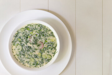 Cold soup in a deep white plate on a white table. Okroshka, a traditional dish of Russian cuisine. Top view. Copy space.