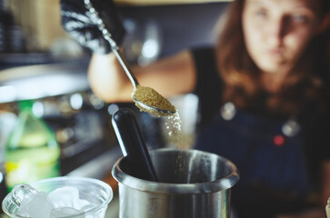 Bartender wearing medical latex black gloves,making mojito cocktail.Process of bartending in bar,pouring a tablespoon of brown sugar in shaker.Blurred image, selective focus