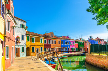 Fototapeta na wymiar Colorful houses of Burano island. Multicolored buildings on fondamenta embankment of narrow water canal with fishing boats and wooden bridge, Venice Province, Veneto Region, Northern Italy