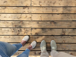 Two people are standing on a wooden surface. Top view of feet shod in light summer shoes