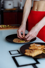 Woman's hand decorates pancakes with a fruits kiwi and banana. Black plate, white table