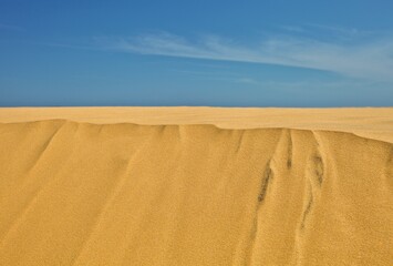 Sand dune against bright blue sky and sea. View on the sandy slope of the sand dune in hot sunny day. Sand dune surface close-up. Sand texture. Sand pattern full frame photography. Sand ripples.