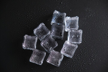 Ice cubes on a reflecting table with drops of water on a black background