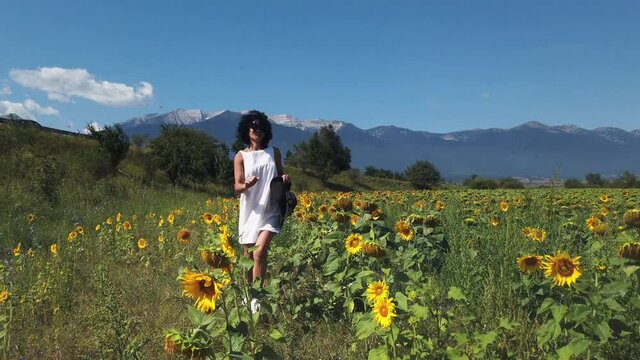 Happy young woman with hat running in the field of sunflowers, arm raised, slow motion