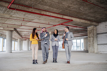 Two muslim investors walking around building in construction process and talking with real estate agents about investment.