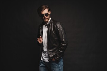 Fototapeta premium Fashion man, Handsome serious beauty male model portrait wear sunglasses and leather jacket, young guy over black background