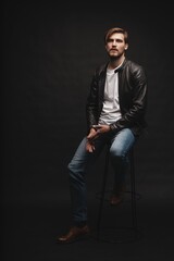 Fototapeta premium Fashion man, Handsome serious beauty male model portrait wear leather jacket, young guy over black background