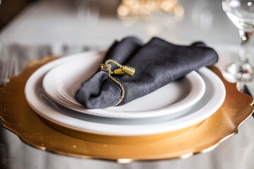 Guardanapos de tecido preto com enfeites dourados, dentro do prato. © Angela