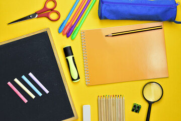 
Back to school. Varied school supplies from small blackboard with chalks and daily supplies at school, on yellow background