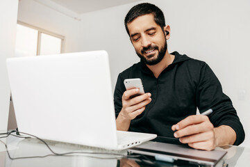 Designer working from home using laptop and tablet. Checking something on the phone