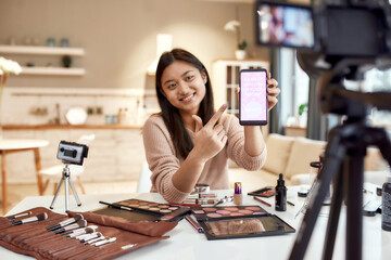 Just try. Beauty blogger woman filming, advertising app on camera, holding smartphone. Makeup...