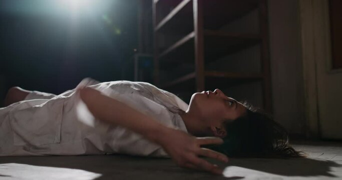 Exhorcist girl in white shirt convulsing on old wooden floor. Scary female demon awakening in haunted hallway - halloween costume, horror movie 4k footage