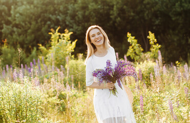 Charming girl in a white dress with a bouquet of lupines in her hands.