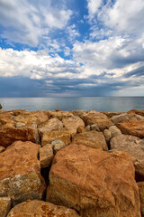 Fototapeta na wymiar Colorful stones on a shore with fluffy clouds at the horizon. Vertical view