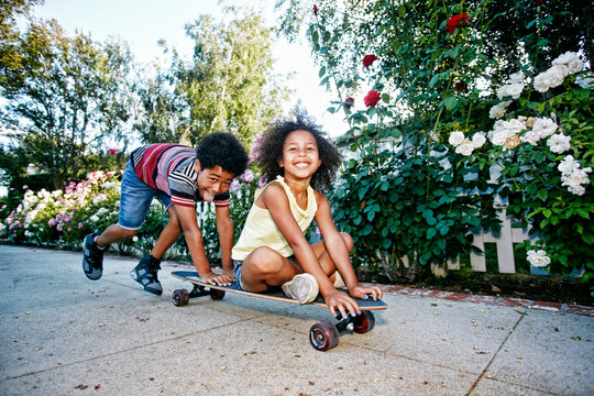 Mixed Race boy pushing sister on skateboard on sidewalk