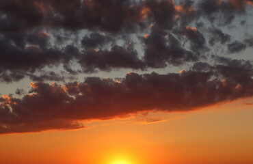Summer sunset sky with orange and dark blue clouds
