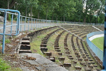 Obraz premium a football stadium tribune in disrepair or decayed in a provincial town in Eastern Europe. Wooden seats were removed because they were rotten and the space between rows is infested with weed. 