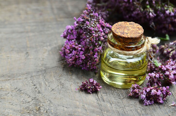 Oregano essential oil in a glass bottle with fresh blooming herb twigs on a wooden background. Aromatherapy, natural cosmetics,spa or bodycare concept.Selective focus.