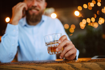 A young handsome caucasian businessman with a beard is sitting in a cafe drinking whiskey and working on a laptop. Work in a restaurant
