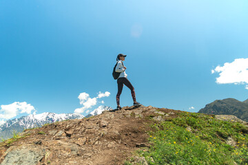 Young woman with backpack standing on top of cliff edge and looking to landscape. Hiking and travel in mountain