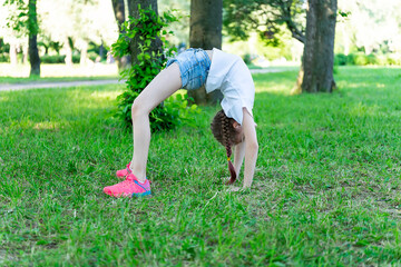 Fototapeta na wymiar Girl child performs an exercise bridge on the grass in the park