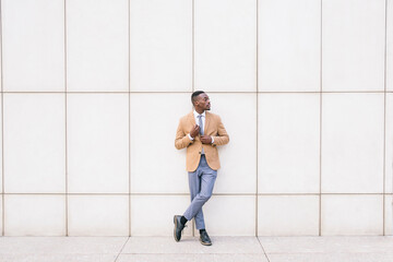 Young businessman leaning against a wall looking sideways