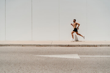 Barechested male athlete running on pavement with arrow sign on the road