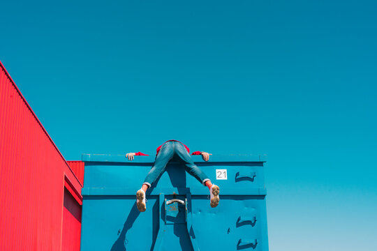 Young man hanging over edge of blue container, rear view