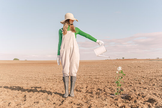 Woamn standing on barren field, watering flower