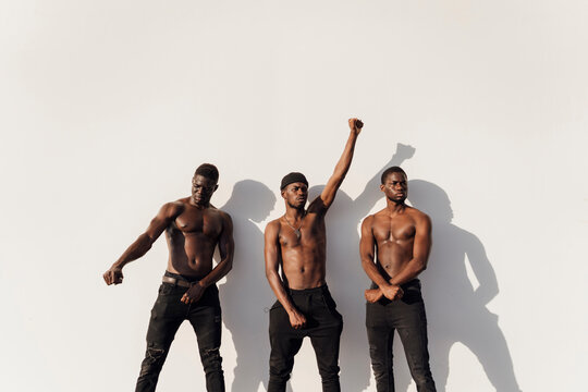 Three men raising fists in protest, standing against white wall
