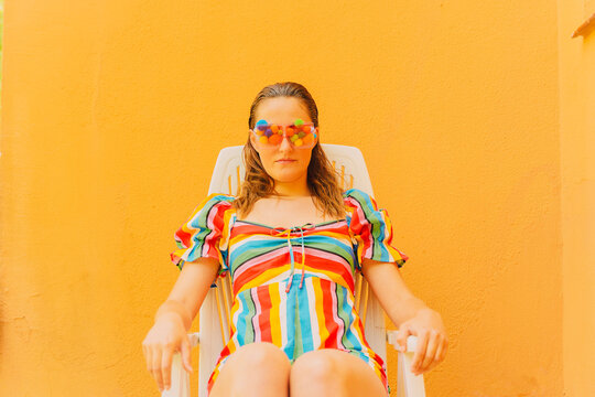 Portrait of woman wearing glasses with colourful pom poms covering her eyes relaxing on plastic chair