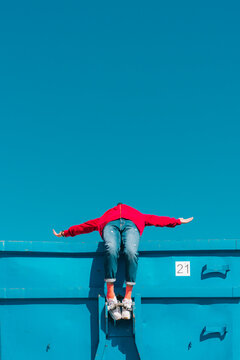 Young man relaxing on blue container, leaning backwards over edge