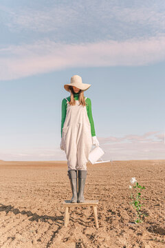 Woamn standing on stool, watering flower on barren field