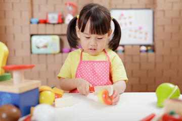 toddler girl pretend play food preparing role against cardboard blocks kitchen background