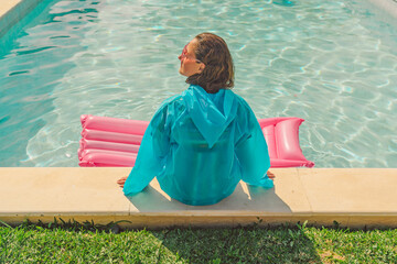 Back view of woman in blue rain coat sitting at poolside