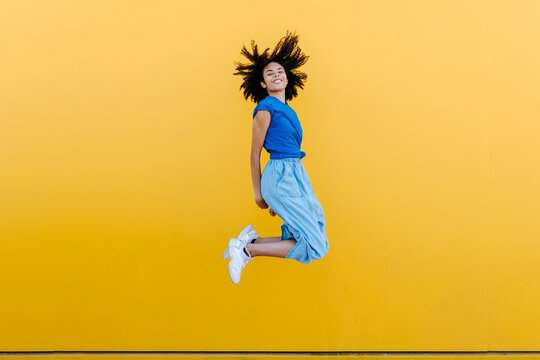 Pretty woman jumping for joy in front of yellow wall