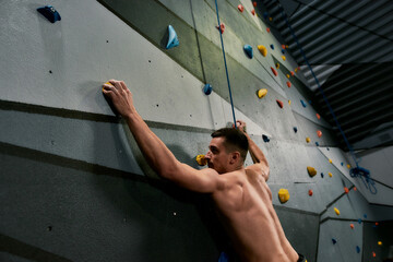 Fototapeta na wymiar Young athletic man looking focused, while training on the artificial climbing wall indoors