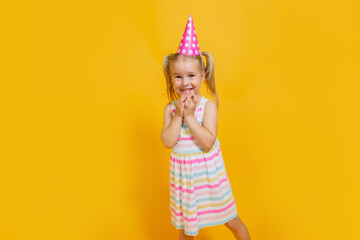 Happy birthday child girl with two ponytales in pink cap on colored yellow background. Copyspace.