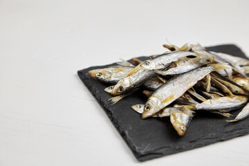 Small dried sardelle or tulka fish on slate board over white background.