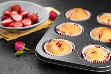 Homemade muffins with fresh strawberries on dark concrete background