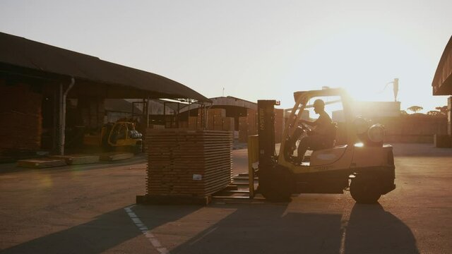 empilhadeira carregando t&aacute;buas de madeira, contra luz do sol