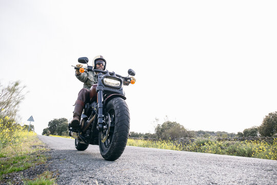 Male Biker Wearing Helmet Riding Motorcycle On Road Against Clear Sky