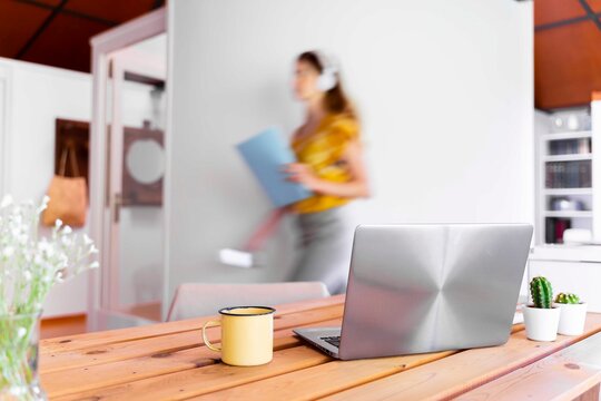 Laptop and mug on desk with blurred motion of woman in background