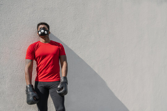 Portrait of a sportsman wearing face mask and boxing gloves at a wall