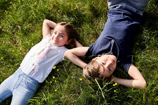 Smiling girl lying by brother on grass during sunny day