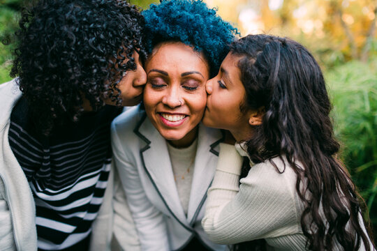 Loving children kissing on smiling mother's cheeks in park