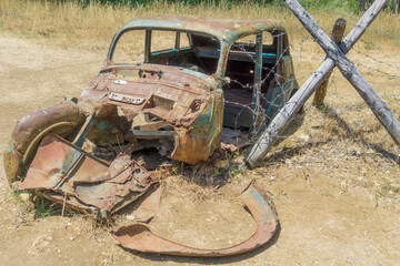 Old collapsed retro car thrown on a rusty field after the war. broken, barbed wire with obstruction
