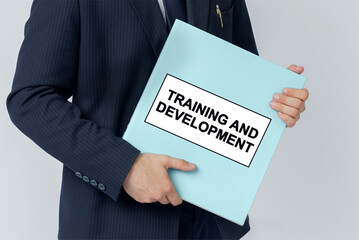 A businessman holds a folder with documents, the text on the folder is - TRAINING AND DEVELOPMENT
