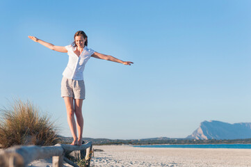Smiling woman balancing on fence on the beach, Sardinia, Italy
